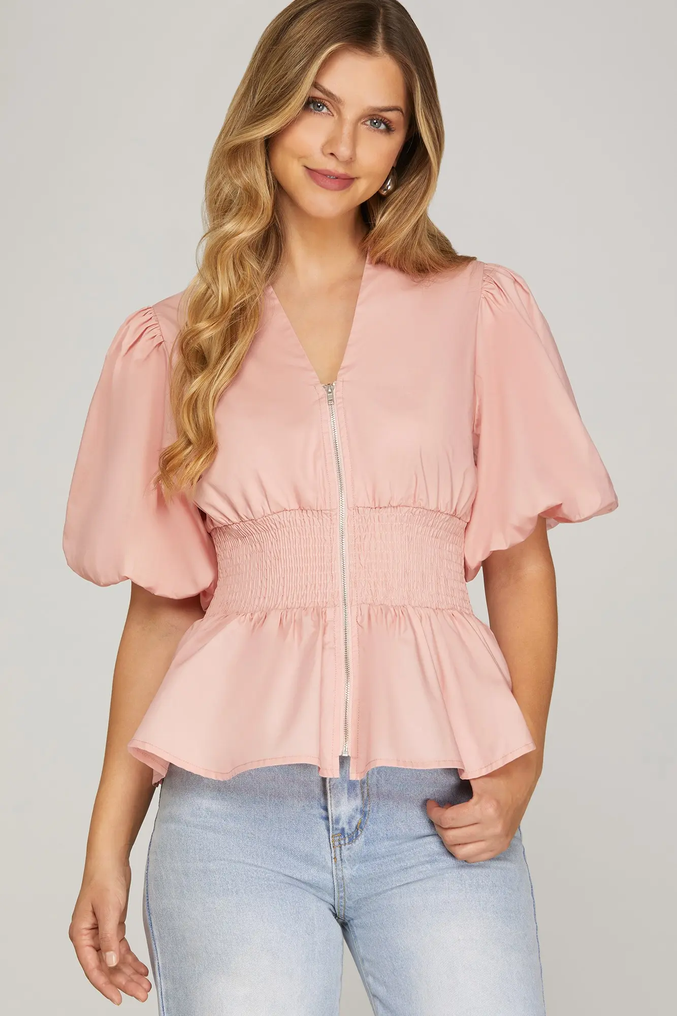 Model wearing pink puff-sleeve smocked zip-front top