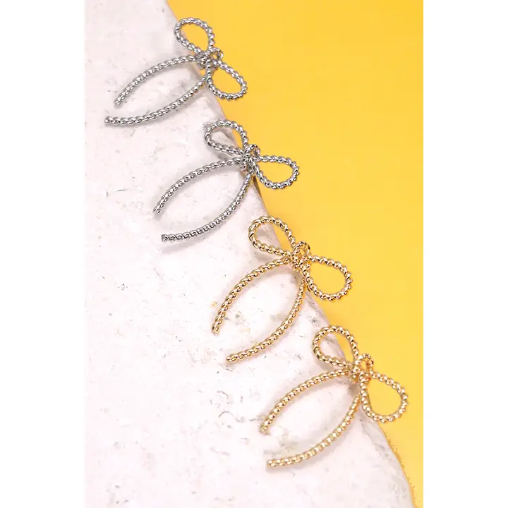 Gold rope bow jewelry with multiple bow charms on a diagonal line against a white and yellow background.