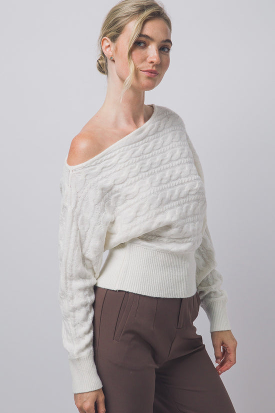 Angled view of ivory cable-knit off-shoulder sweater