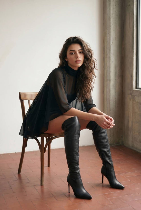 Seated view of black cape-overlay satin mini dress showing sheer shoulder drape