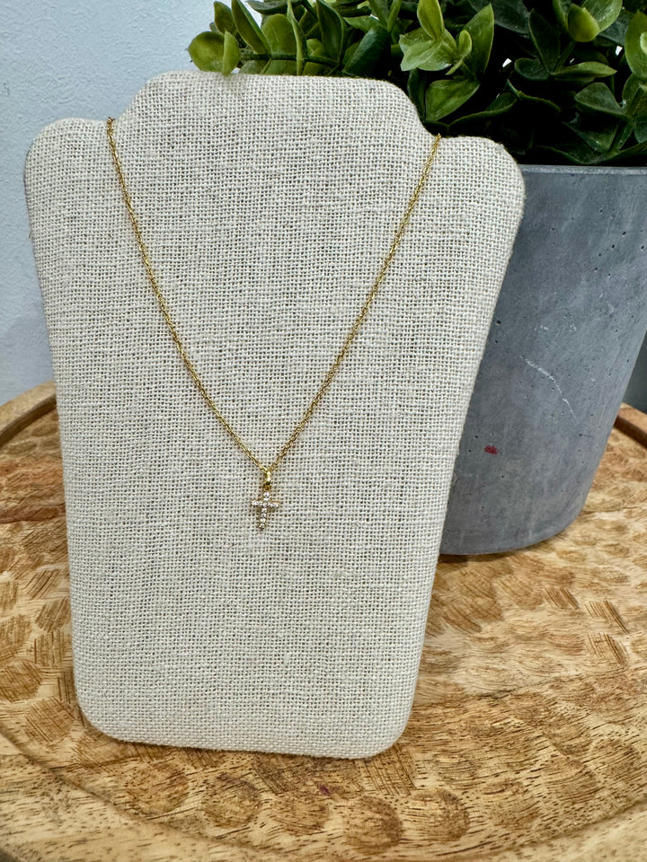 Gold necklace on a white bust with a wooden surface and plant in the background