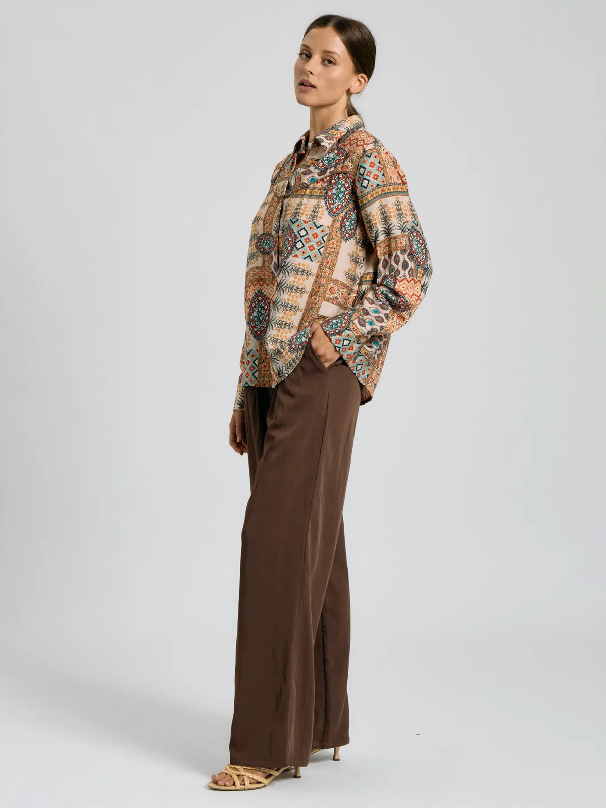 Full-length styling of patchwork-print shirt with brown trousers