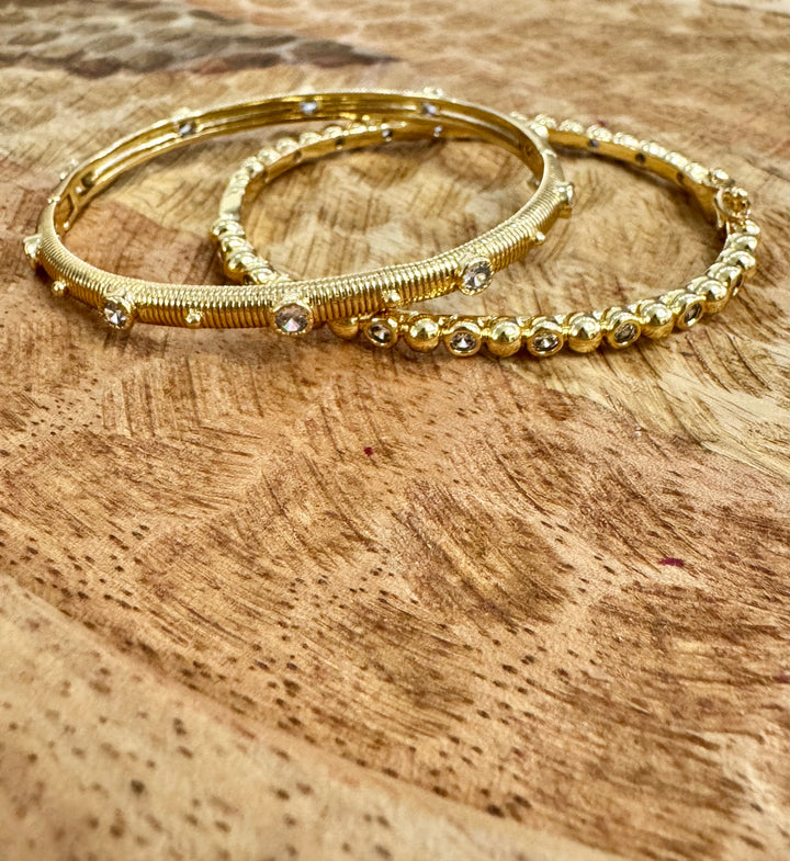 Two gold bangles with bead detailing on a wooden surface