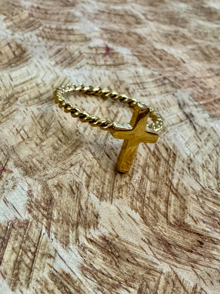 Gold ring with a cross pendant on a textured wooden surface